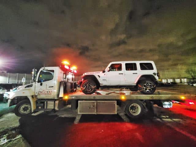 White Jeep being towed on a flatbed tow truck at night in the GTA