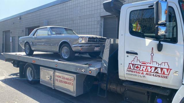 1965 Ford Mustang Coupe being transported on a Norman Towing flatbed truck