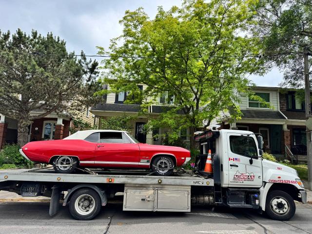 A gleaming red vintage car, possibly a convertible, is transported on a professional tow truck, ready for its next destination.