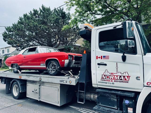 A vibrant red classic car is towed on a flatbed truck.