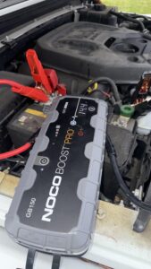 Professional NOCO Boost Pro GB150 jump starter connected to a white Jeep Wrangler JL battery with 14.4V digital display reading.